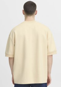 Béžové oversized tričko s krátkymi rukávmi a ribbovaným výstrihom; hladká textúra, uvoľnený strih; výnimočné svojou jednoduchosťou a jednofarebnosťou.