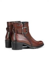 Botas de cuero marrón hasta el tobillo con punta redondeada, detalle de hebilla en el lateral, tacón texturizado y suela de goma negra. Acabado suave con costuras mínimas.