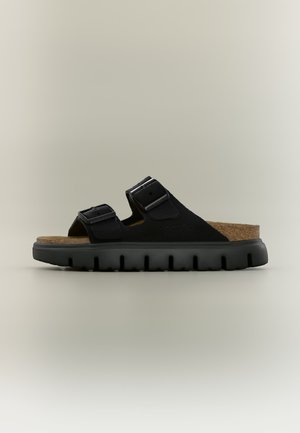Sandalo nero con due cinturini regolabili con fibbia, plantare in sughero e suola spessa in gomma nera con scanalature profonde, mostrato di profilo laterale.