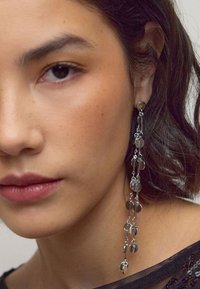 Silver dangle earrings with circular discs, featuring a cascading design and fine chain links, complementing a black textured top.