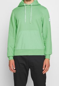 Felpa verde realizzata in morbido materiale, con tasca a marsupio, cappuccio regolabile con cordino e polsini e orlo a costine.