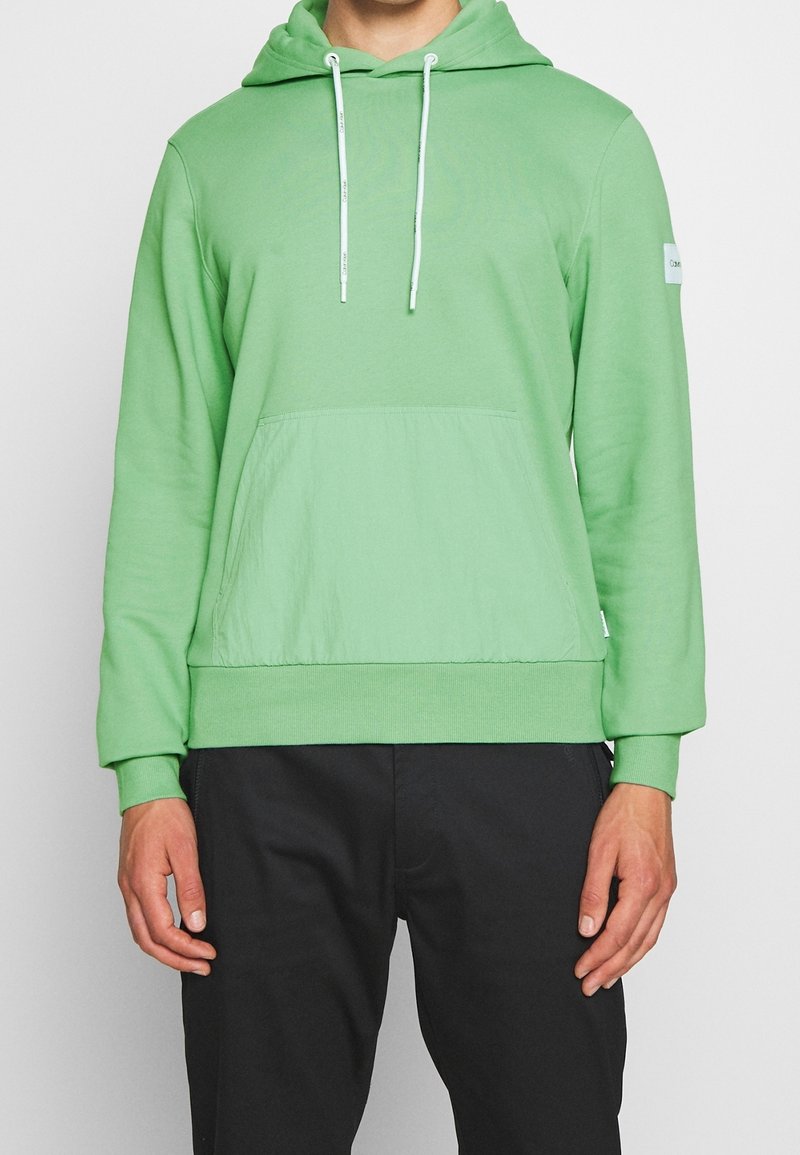 Felpa verde realizzata in morbido materiale, con tasca a marsupio, cappuccio regolabile con cordino e polsini e orlo a costine.