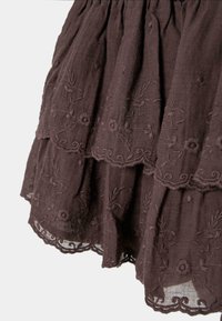 Tissu brun foncé avec motifs floraux brodés en couches et bords festonnés sur un matériau léger et texturé.