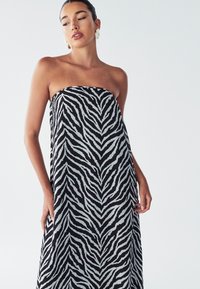 Maksi haljina bez naramenica u crnoj i svijetlo sivoj boji sa uzorkom zebra, koja se odlikuje slobodnim krojem i glatkim, laganim materijalom.