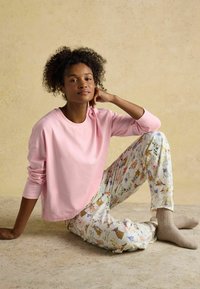 Roza majica z dolgimi rokavi, ohlapne hlače s pisanimi živalskimi vzorci in bež pletene nogavice, sedeča na teksturirani površini.