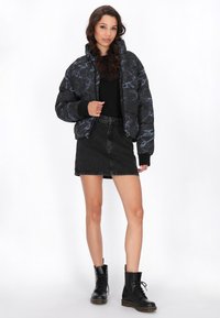 Zwarte bomberjack met marmerpatroon, zwarte top, denim minirok en zwarte veterschoenen. Met een gevoerd ontwerp en ribbelmanchetten.