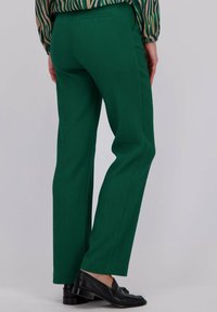 Groene getextureerde broek met een recht model, voorzien van een achterzak, gecombineerd met zwarte loafers, voor een neutrale achtergrond.