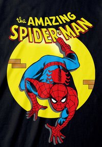 Černé tričko s potiskem kresleného Spider-Mana v modro-červeném obleku, umístěné na žlutém kruhu s textem "úžasný SPIDER-MAN" nahoře.