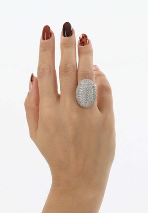 Silberner Ring mit einer ovalen Fläche, die mit kleinen klaren Edelsteinen bedeckt ist, präsentiert an einer Hand mit verschiedenen Nageldesigns und Farben.