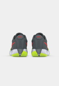 Grijze sportwanden met neon gele zolen. Opvallende rode accenten op de hiel en zijkant, textuur mesh bovenwerk en achterventilatie details.