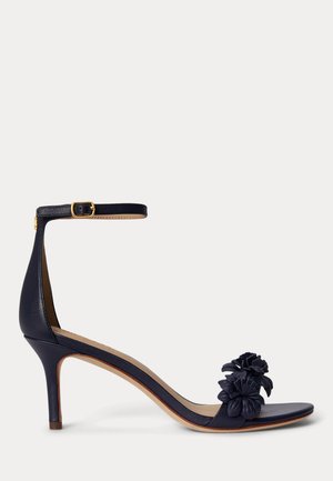 Σανδάλι με ψηλό τακούνι σε ναυτικό μπλε χρώμα, με λουράκι στον αστράγαλο και αγκράφα, ανοιχτή μύτη και δύο διακοσμητικά λουλούδια στο μπροστινό λουράκι.