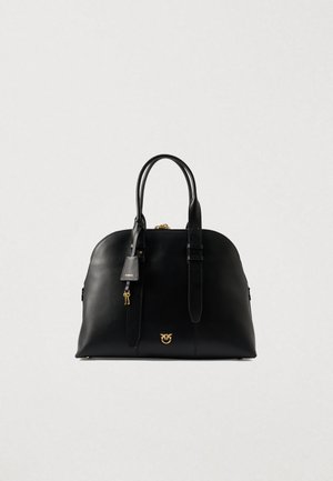 Black leather handbag with double handles, gold-tone logo emblem, and attached key charm on plain light background.