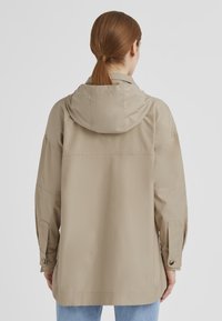Beige, wasserabweisende Jacke mit Kapuze, lockerer Passform und verstellbaren Bündchen. Ausgestattet mit flachen Nähten und einer glatten, matten Textur.