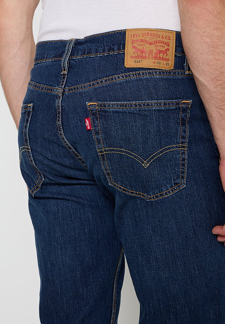 Blaue Stretch-Jeans mit regulärer Passform, ausgestattet mit gelben Nähten, zwei Gesäßtaschen und einem braunen Lederetikett mit dem Levi's-Logo am Bund.
