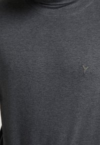 Maglione a collo alto grigio scuro realizzato in tessuto morbido, con un piccolo logo metallico sulla zona del petto, design minimalista senza pattern.