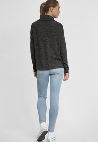 Maglione nero melangiato rilassato con collo a cascata, abbinato a jeans skinny azzurri e sneaker bianche, visto da dietro.