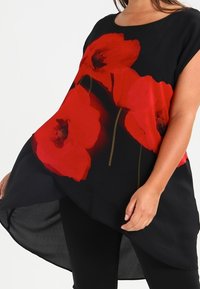 Černý tunikový top s velkými kv�ětinovými vzory červených máků, kulatým výstřihem a asymetrickým lemem. Vyrobeno z lehké tkaniny s splývavým střihem.