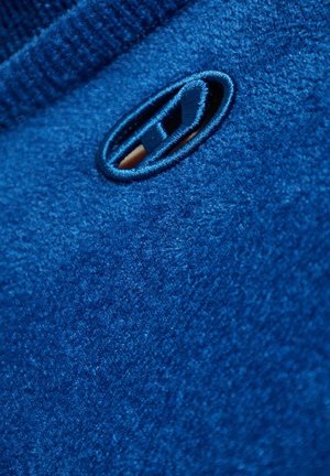 Indumento in pile blu con una texture liscia, scollo a coste e un dettaglio cucito prominente a forma ovale vicino al colletto.