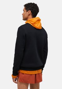 Melnā sporta krekls ar oranžu kapuci, virsū valkāts ar atbilstošā oranžā krekla. Materiāls izskatās mīksts, un dizains ir ikdienišķs ar garām piedurknēm.