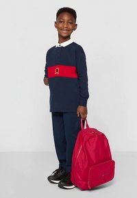 Marineblå langermet polo med rød stripe og emblem, kombinert med matchende marineblå bukser og en knallrosa ryggsekk. Sorte joggesko fullfører antrekket.