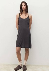 Dark gray sleeveless dress with a scoop neckline, made of a smooth material, falling just above the knee. Paired with fuzzy socks and clogs.