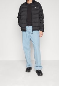 Svart puffjacka med horisontell sömnad, dragkedja och ståkrage, ihop med ljusblå denimjeans och svarta sneakers.
