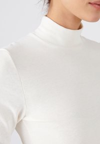 Maglione a collo alto bianco a coste, design aderente, texture morbida, con collo alto e maniche lunghe, che mostra cuciture e dettagli minimi.
