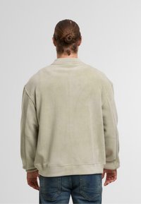 Fleece sweatshirt in een lichtgroene tint, met een ontspannen pasvorm, verlaagde schouders en ribgebreide manchetten. Glad textuur, minimalistisch ontwerp.