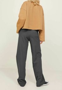 Afgekruimd bruine sweatshirt met brede mouwen, gecombineerd met donkergrijze, losse broek. Converse schoenen zijn gedeeltelijk zichtbaar.