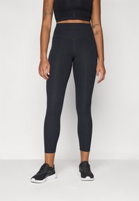 Leggings neri a vita alta con una trama liscia e elastica e cuciture piatte, abbinati a scarpe da ginnastica nere con suola bianca.