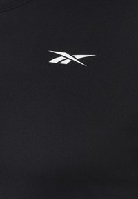 Camiseta atlética negra con un logo blanco de Reebok. La tela es suave y ajustada, con un escote redondo y mangas cortas.