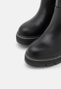 Bottes noires à la cheville en cuir texturé. Bout ronds, semelles en caoutchouc avec traction, et coutures contrastantes le long du bord.