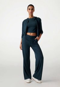 Zestaw sportowy w ciemnym morskim kolorze, składający się ze skróconego topu i luźnych spodni. Zawiera kurtkę na zamek z kieszeniami, wykonaną z miękkiego materiału.