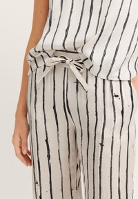 Leichtes Blusen- und Hosen-Set mit schwarzen Streifen auf einem cremefarbenen Hintergrund. Das Outfit hat einen gebundenen Taillendetail und eine glatte Textur.