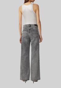 Un débardeur blanc à côtes associé à un jean gris à taille haute et jambes larges. Le jean présente une décoloration subtile, deux poches arrière et une ceinture noire.