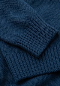 Königsblauer Strickpullover aus Stoff mit gerippten Bündchen und glatter Textur, der detaillierte Nähte zeigt und eine Nahaufnahme des Strickmusters bietet.