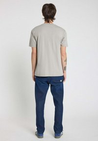 Un t-shirt gris à manches courtes associé à un jean bleu. Le t-shirt présente un design simple, tandis que le jean a une coupe décontractée avec des coutures visibles.