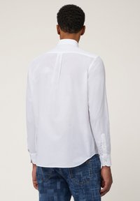 Chemise blanche à manches longues en tissu léger, avec un empiècement au dos, un ourlet arrondi et des poignets à boutons.