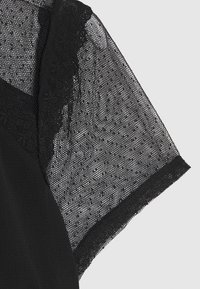 Zwart kledingstuk met een textuurrijk kanten overbedekking op de mouw. De basis heeft een gladde afwerking met een subtiele glans, wat een contrast creëert.