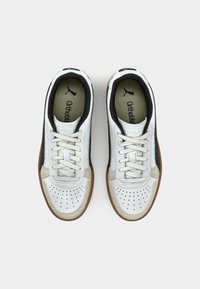 Scarpe atletiche in pelle bianca con punta perforata, dettagli grigi e suole in gomma marrone. Caratterizzate da lacci e una fodera nera imbottita.