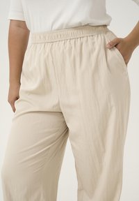 Svijetlosmeđi, lagani hlače s elastičnom waistband-om i bočnim džepovima, s glatkom, blago teksturiranom tkaninom.