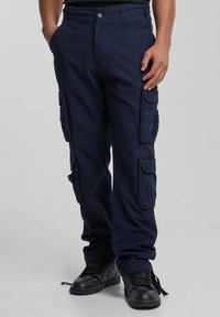 Marinblå cargobyxor i bomullsblandning med flera fickor, slitstarkt tyg, elastiska mudd och förstärkta sömmar; kombinerade med svarta sneakers.