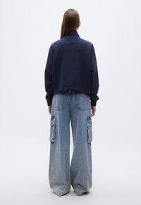 Μπλε σκούρο cropped φούτερ με ψηλό γιακά, σε συνδυασμό με ανοιχτό μπλε παντελόνι καμπάνα με τσέπες μπροστά και υφασμάτινη υφή.