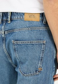 Niebieskie dżinsy z denimu z skórzaną łatką marki, kontrastowymi szwami, tylną kieszenią oraz prostym krojem.