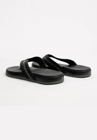 Chanclas negras con tiras texturizadas y una suela gruesa. Las tiras presentan un sutil detalle en zigzag, complementando la suave suela.