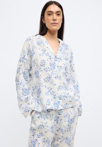 Ensemble de pyjama fleuri en tissu léger, avec des imprimés botaniques bleus sur fond crème, fermeture à boutons et coupe décontractée.