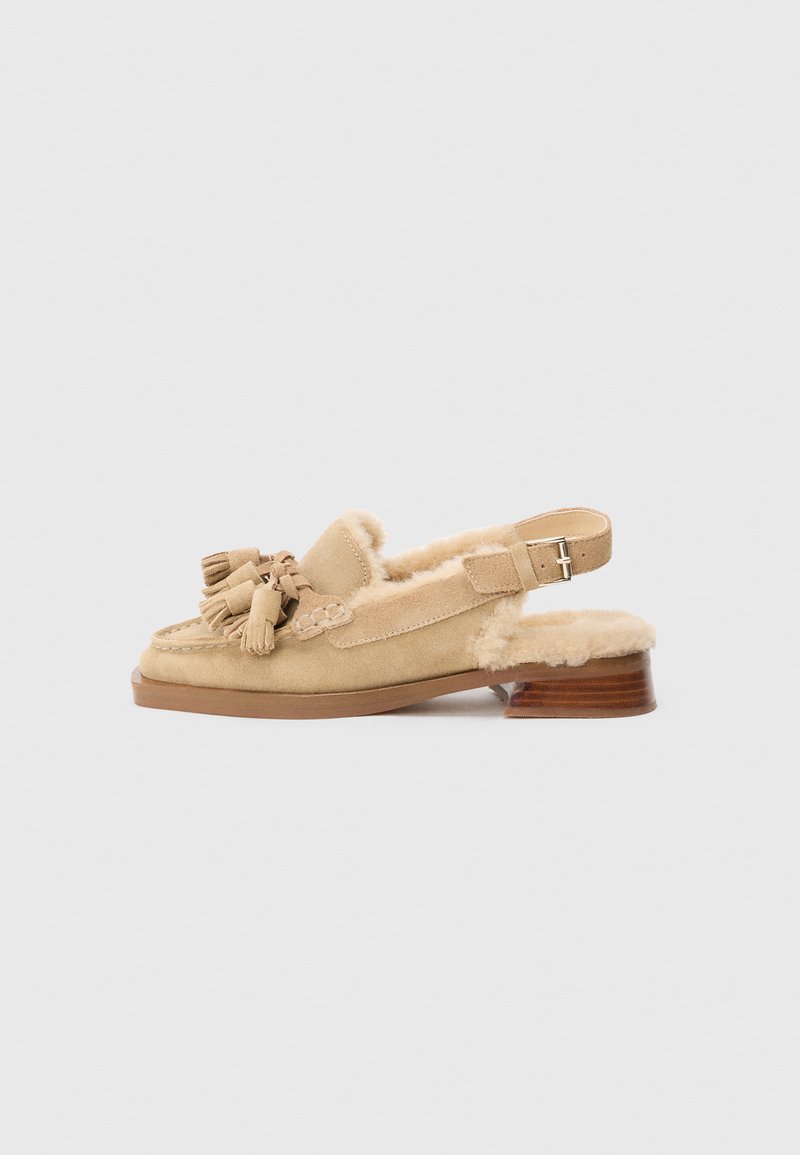 Beige suède slingback schoen met een ronde neus, schapenvacht voering en decoratieve kwastjes. Heeft een houten blokhak.