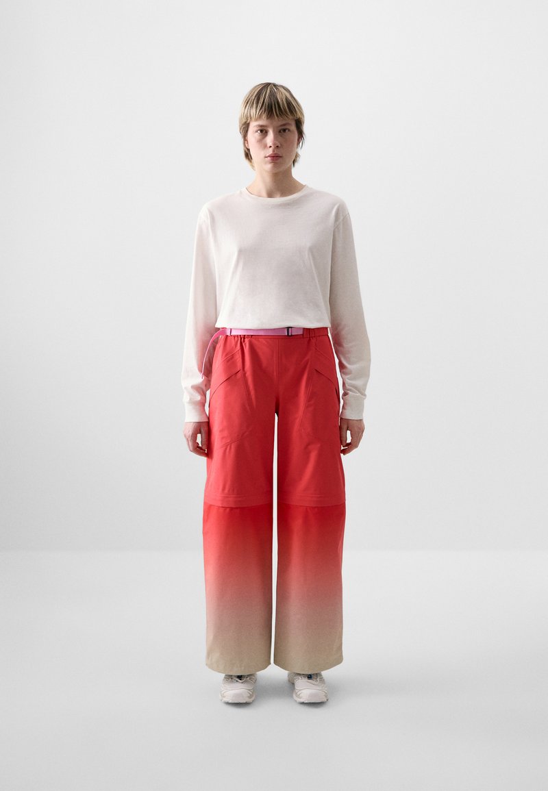 Rode broek met een ombre-effect dat overgaat in lichtbeige, met een wijd wijde cut, zijzakken en een roze riem. Draag het met een witte lange mouwen top.