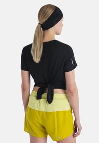 Top negro de manga corta con un detalle de lazo en la parte posterior, combinado con pantalones cortos deportivos amarillos que tienen una cinturilla de color claro y acentos reflectantes.