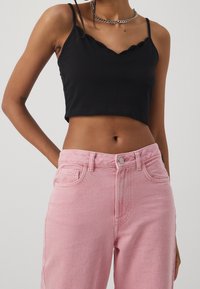 Top corto nero con scollatura ondulata abbinato a jeans di denim rosa chiaro, con dettagli di cucitura e tasche frontali.